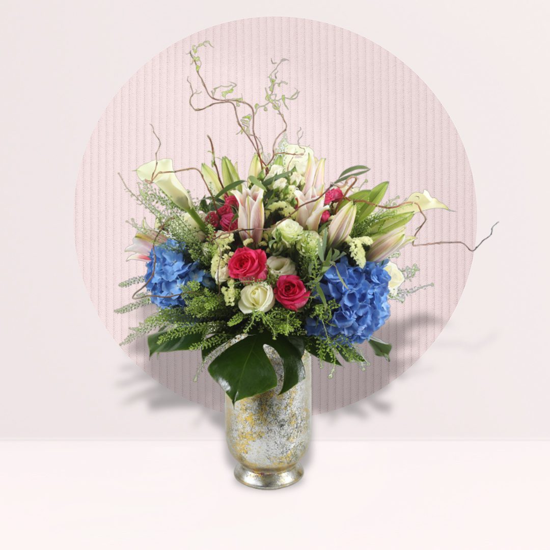 Blushing Blooms in Malaysia Blue hydrangea pink rose lily vase with seasonal fillers and greenery.