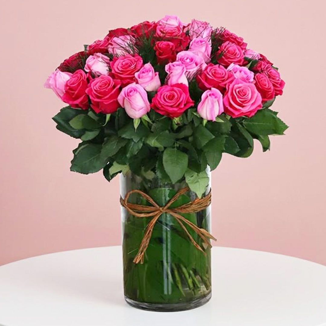 Lavish Pink Roses in Cylinder-156 A light vase filled with vibrant pink and red roses, showcasing a beautiful floral arrangement.