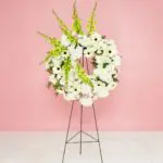 A white floral wreath adorned with green and white flowers, displayed elegantly on a stand.