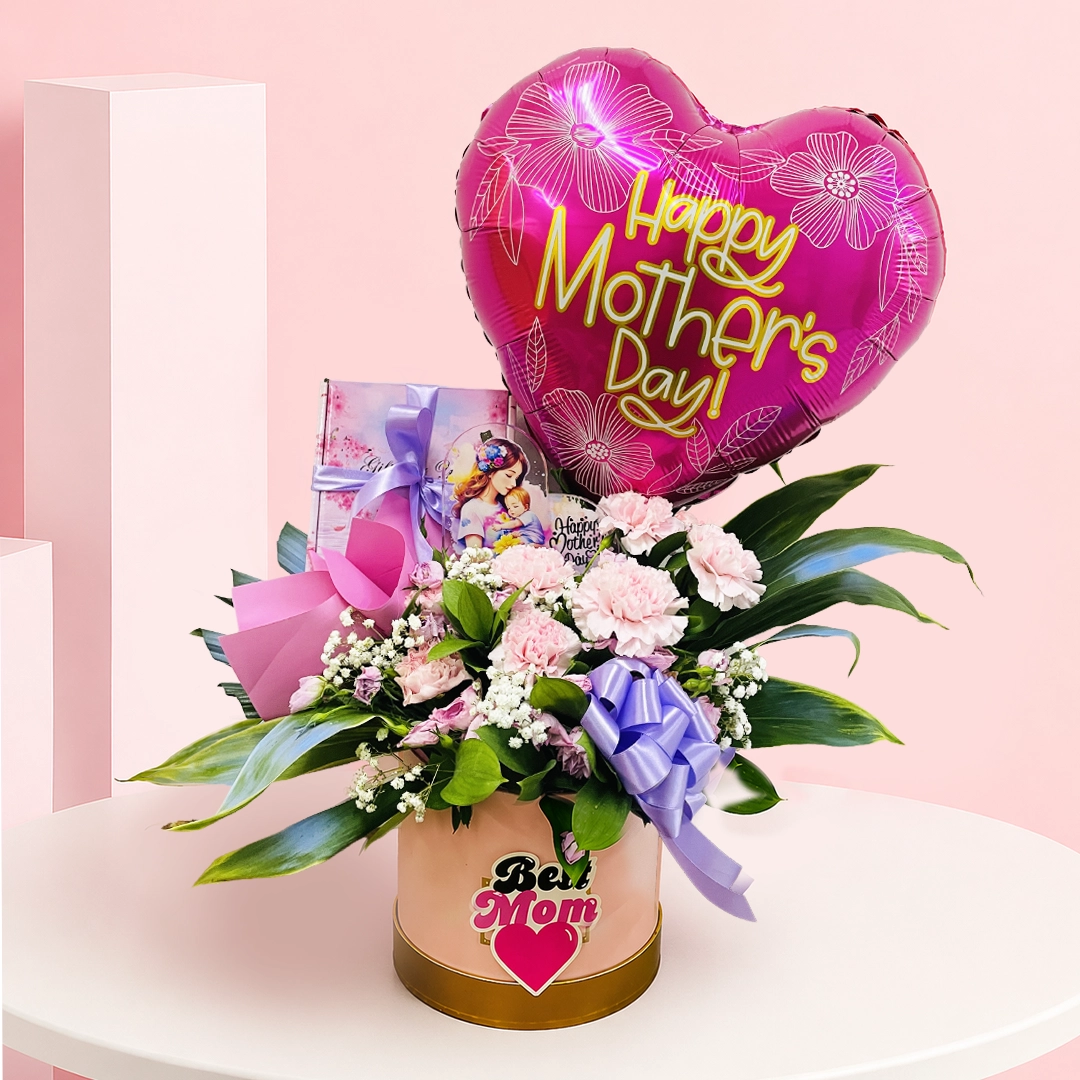 best-mom-blooms_2026 A flower box with pink carnations and baby’s breath, topped with a “Happy Mother’s Day” balloon and greeting card.