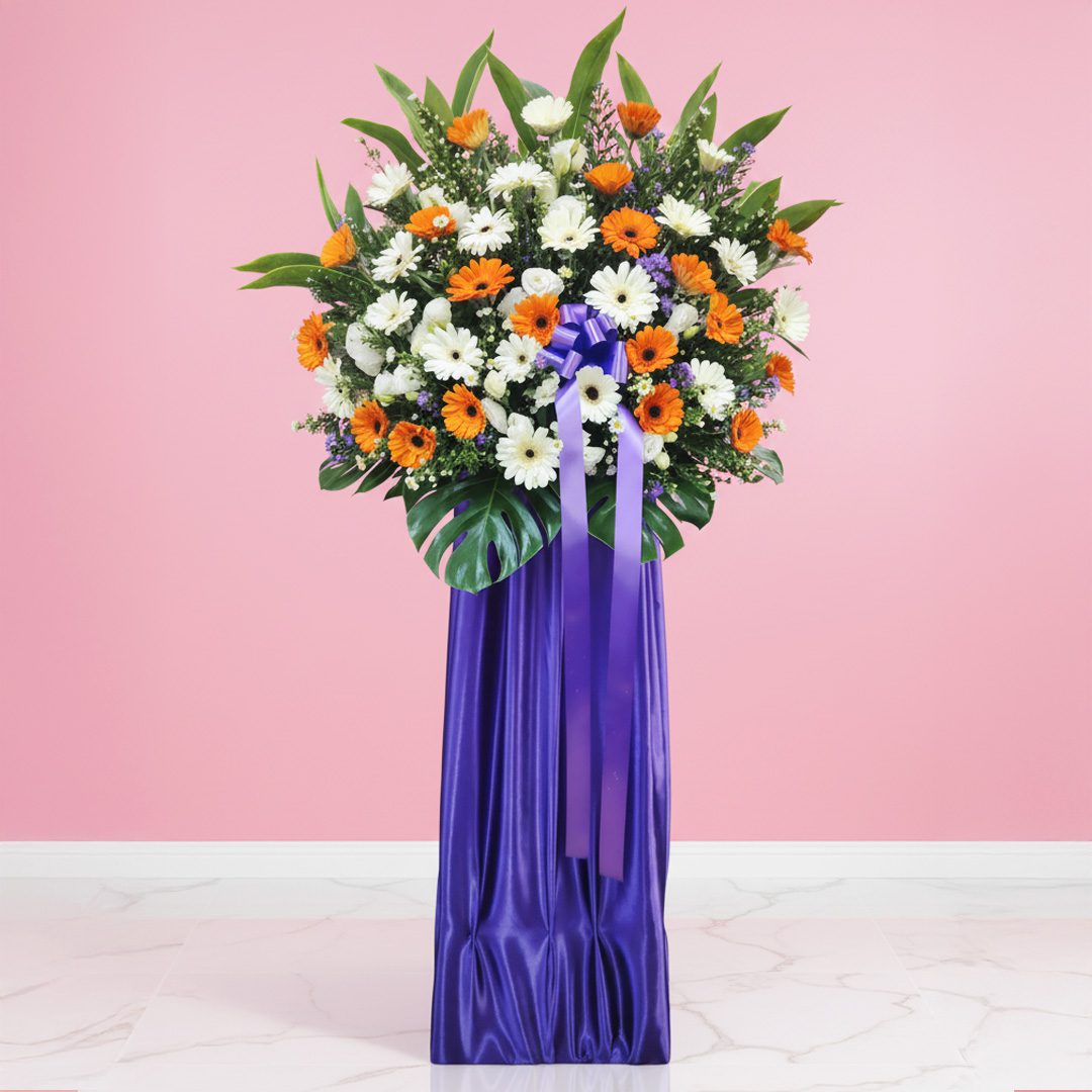 01 Flower stand with orange and white gerberas, greenery, and a purple ribboned base.