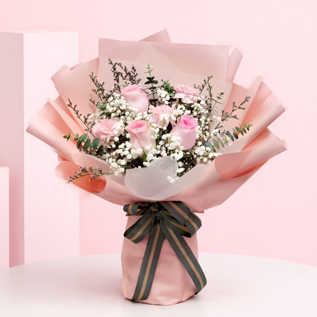 Cupid Blush Peach Wrap Bouquet with Blush pink roses and baby’s breath in a peach wrap, finished with a black ribbon.