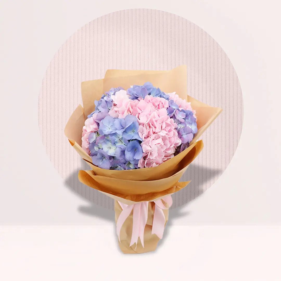 A colorful bouquet featuring pink and blue flowers, elegantly presented in a rustic paper bag.