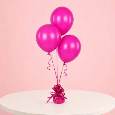 Three fuchsia balloons tied with curly ribbon to a decorative weight, displayed on a white table against a pink background.