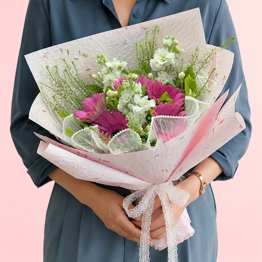 pink-and-white-flower-bouquet Pink gerbera and white matthiola bouquet with fillers and mixed greenery in a pink sheet and tied with a white satin ribbon.