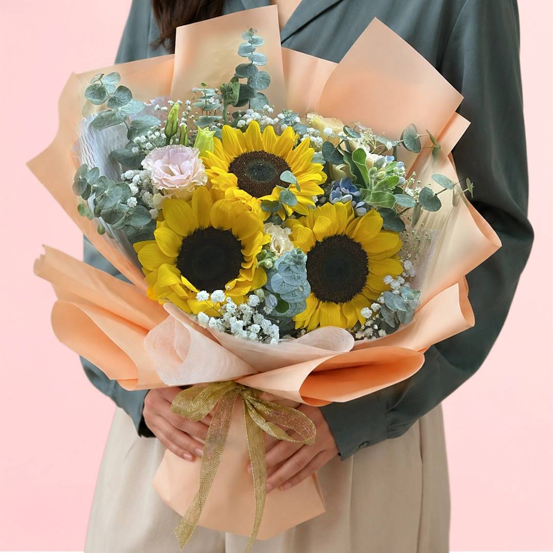 sunshine-garden-blooms Three sunflowers with a lisianthus and fillers beautifully arranged with fresh green fillers wrapped in a pastel sheet.