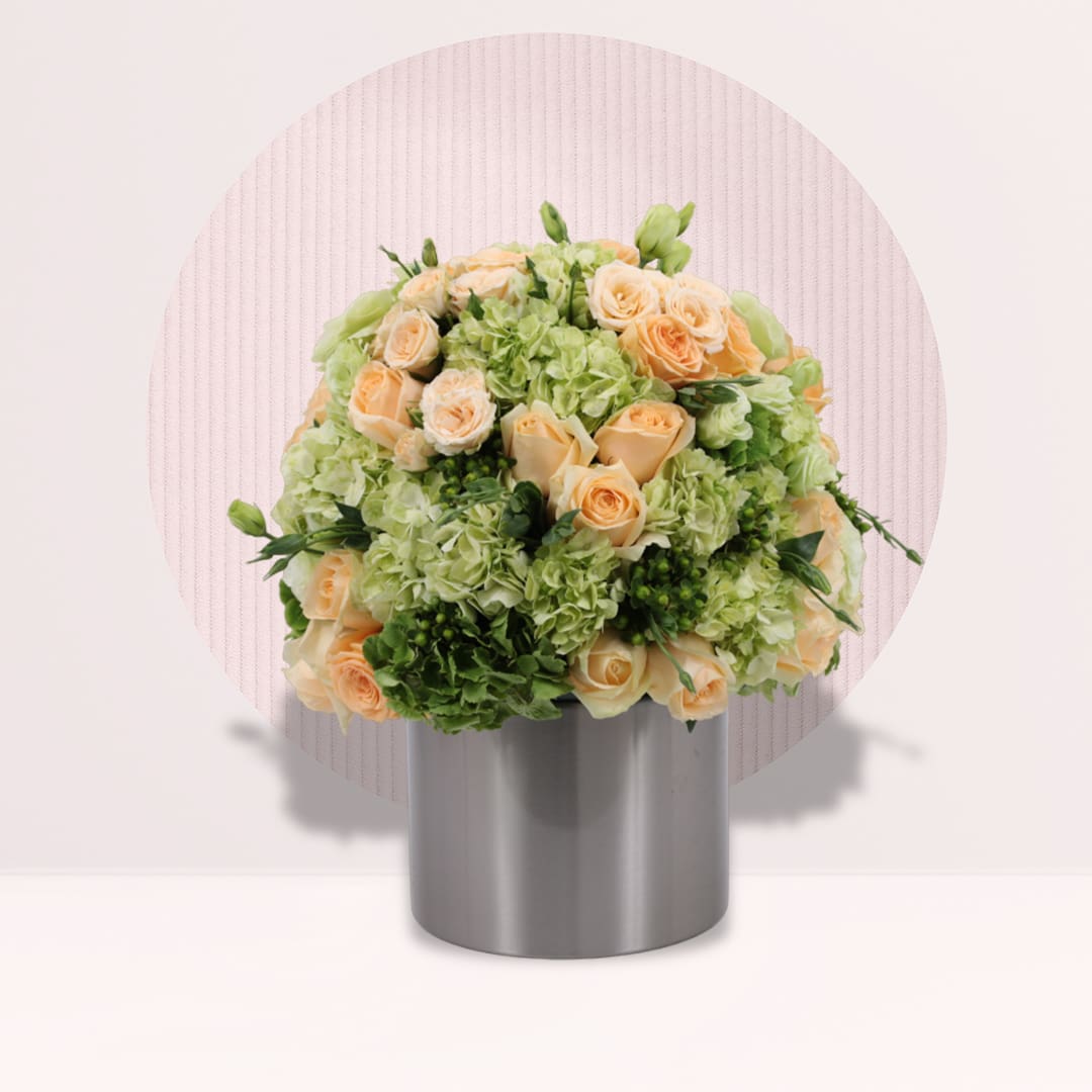 4 (19) Round centrepiece with peach roses, green hydrangeas and spray roses in a grey cylindrical base.
