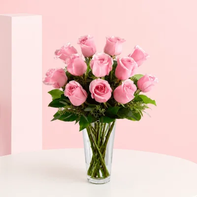 A charming floral arrangement featuring 12 pink roses surrounded by lush greenery, exuding elegance and sweetness.