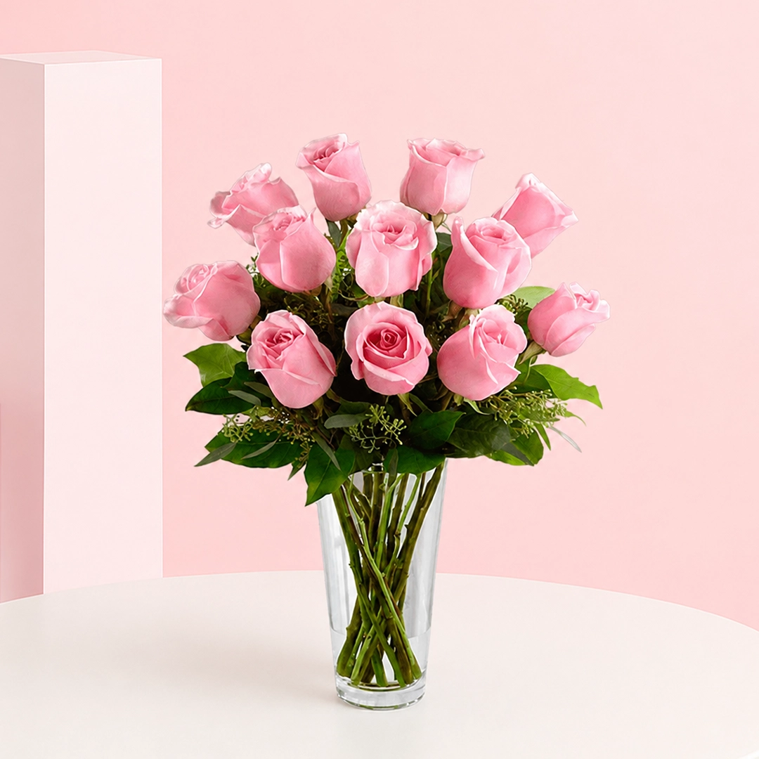 expression-of-pink_2026 A charming floral arrangement featuring 12 pink roses surrounded by lush greenery, exuding elegance and sweetness.