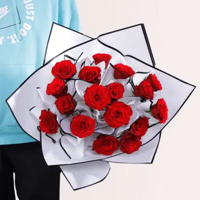 Elegant bouquet of fresh red roses wrapped in white paper with black edges, perfect for gifting.