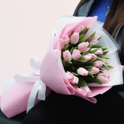 A woman smiling while holding a vibrant bouquet of pink tulips in her hands