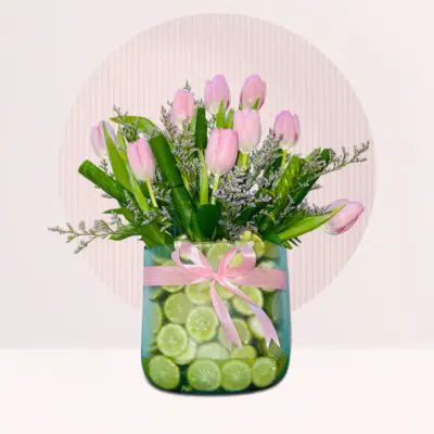 Glass vase of baby-pink tulips with decorative limes and greenery.