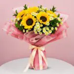 A bouquet featuring sunflowers and daisies in a white table