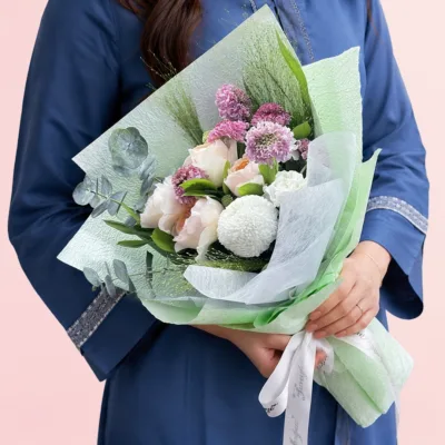 A mixed arrangement with peach roses, white ping pong chrysanthemum, white carnation, fresh fillers, and greenery wrapped as a bouquet.