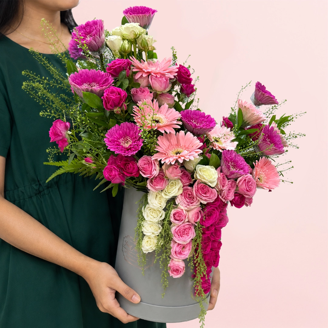 purple-duo-flower-box Black cylindrical flower box filled with purple toned fresh gerberas, spray roses, and seasonal foliage.